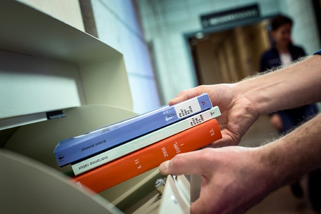 [Photo] Gros plan de mains déposant des livres dans une chute à livre. Bibliothèque de la santé.